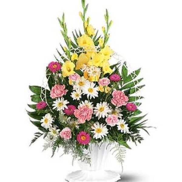 Standing floral arrangement with yellow, pink, and white flowers in a white pedestal vase