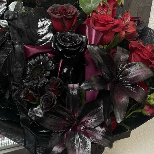 Bouquet of red and black roses with dark lilies in a glass vase