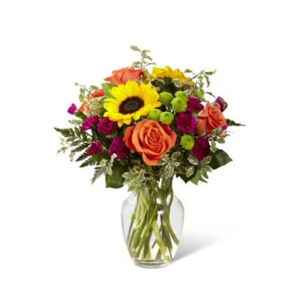 Mixed bouquet with sunflowers, orange roses, and magenta blooms in a glass vase