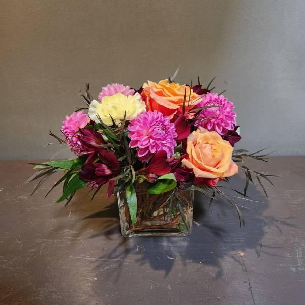 Mixed bouquet of pink, peach, and white flowers in a square glass vase