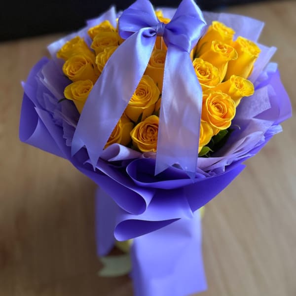Yellow roses wrapped in purple paper with a lavender ribbon bow