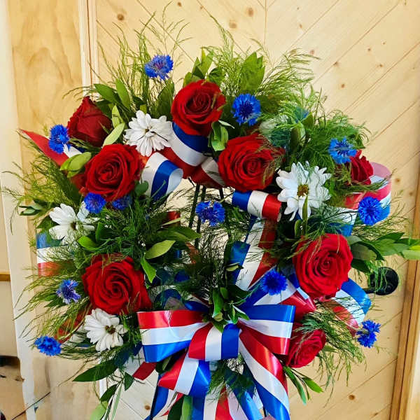 Red roses and white daisies with blue accents on a ribboned standing wreath