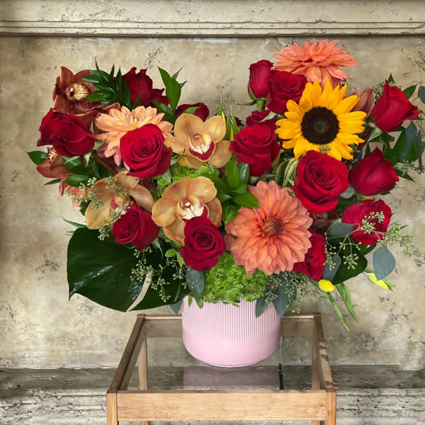 Mixed bouquet with red roses, peach dahlias, and a sunflower in a pink vase