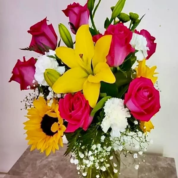 Bouquet of pink roses, yellow lilies, and sunflowers in a glass vase