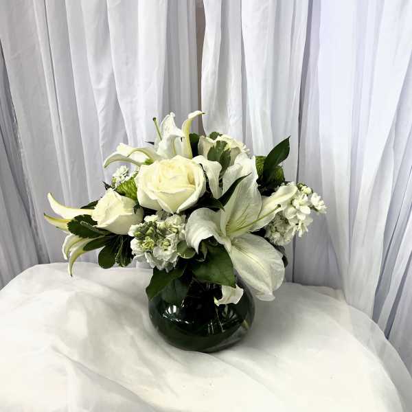 White roses and lilies arranged in a dark glass vase