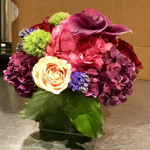 Colorful floral arrangement in a square vase with pink, purple, and yellow blooms