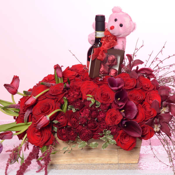 Red rose arrangement with a wine bottle, chocolates, and a pink teddy bear