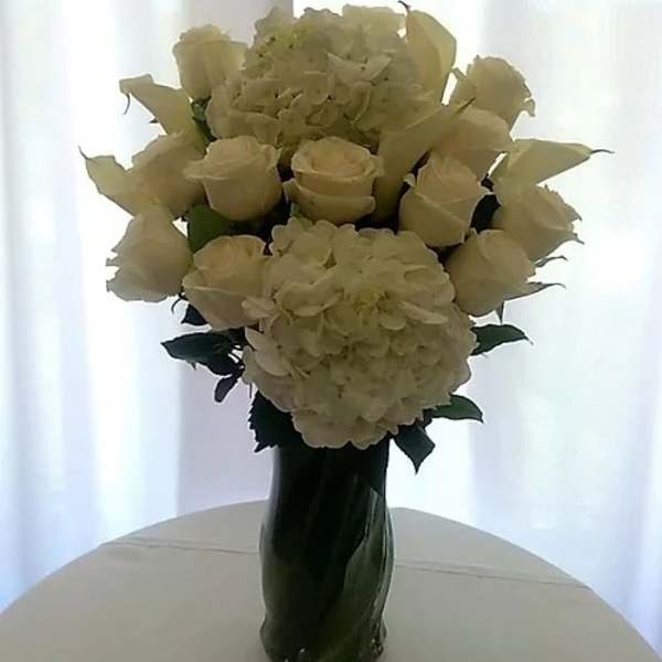 White roses and hydrangeas arranged in a tall glass vase