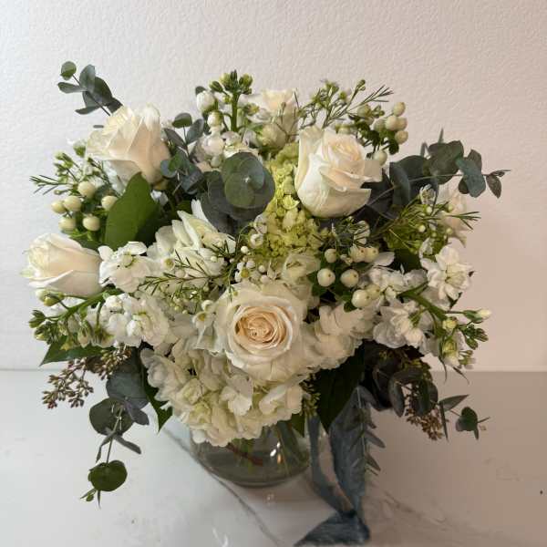 White rose bouquet in a clear glass vase with eucalyptus and small white filler flowers