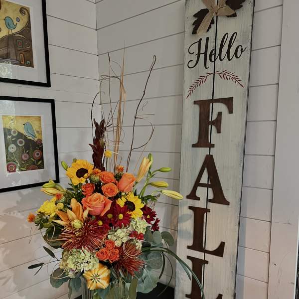 Mixed bouquet in a clear glass vase beside a vertical "FALL" sign