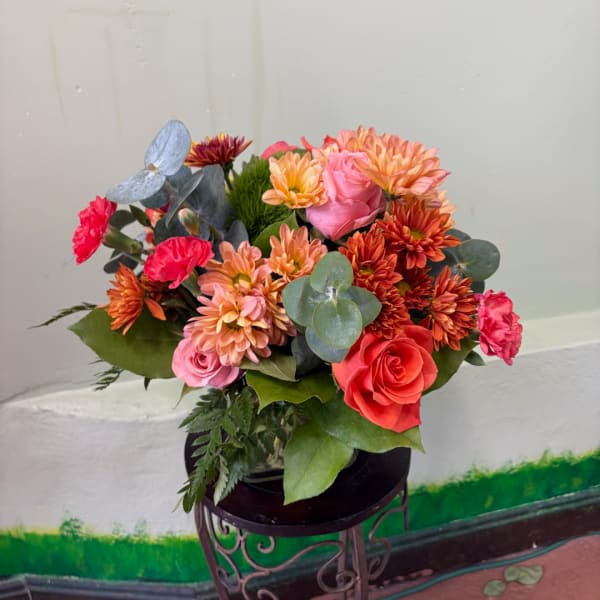 Mixed bouquet of roses, carnations, and mums in a dark vase