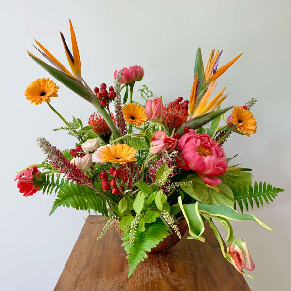 Tropical bouquet with pink peonies, orange gerbera daisies, and bird of paradise in a vase