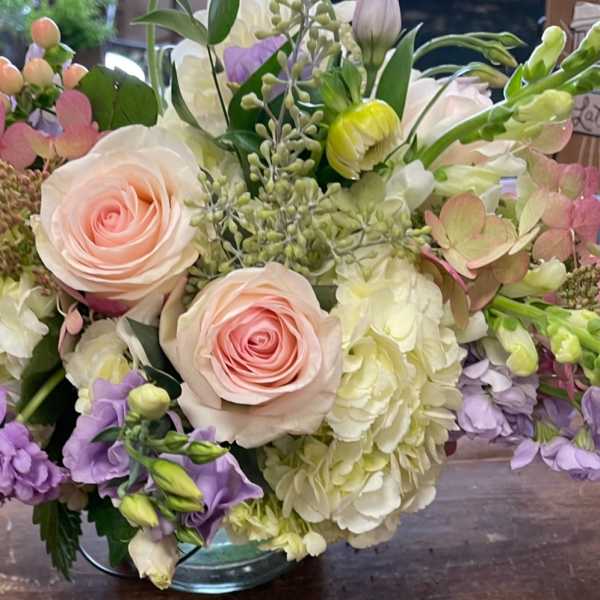 Bouquet of pale pink roses, white hydrangeas, and lavender flowers in a glass vase