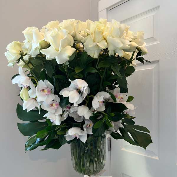 White roses and orchids arranged in a glass vase with a ribbon.