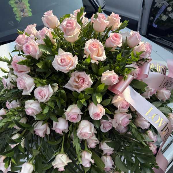 Large bouquet of pale pink roses with ribbon on a car hood