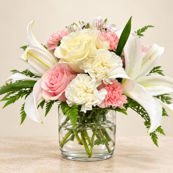 Pink and white bouquet with lilies, roses, and carnations in a glass vase