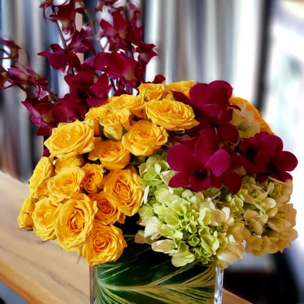 Bouquet of yellow roses, green hydrangeas, and burgundy orchids in a glass vase