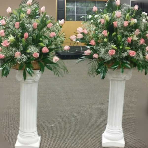 Two pink rose arrangements on white pedestal stands