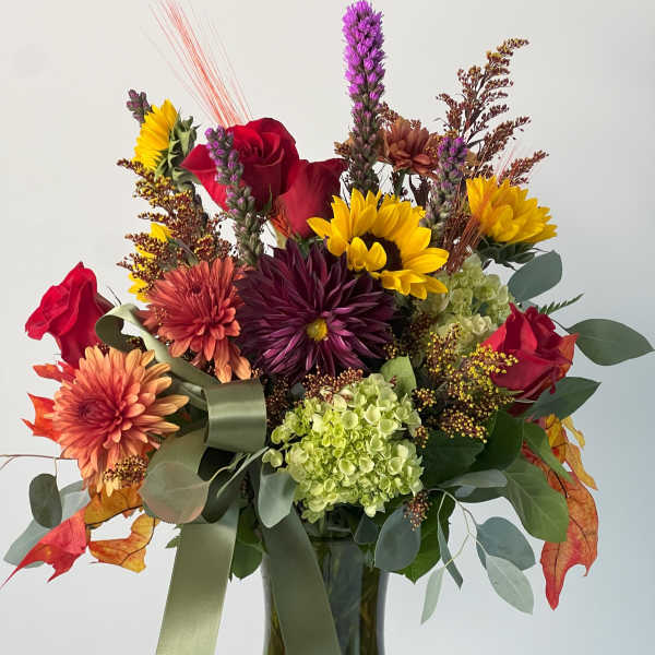Mixed bouquet of sunflowers, roses, and mums in a glass vase