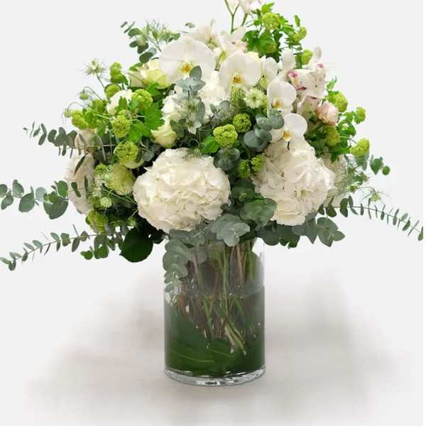 White orchids and hydrangeas in a glass vase with green accents