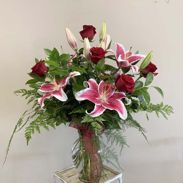 Tall vase arrangement of red roses and pink lilies with a red ribbon bow.
