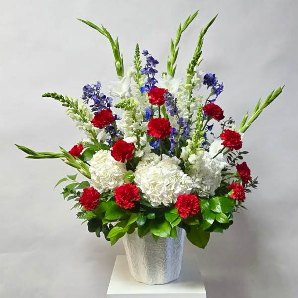 Tall floral arrangement with red, white, and blue flowers in a white vase