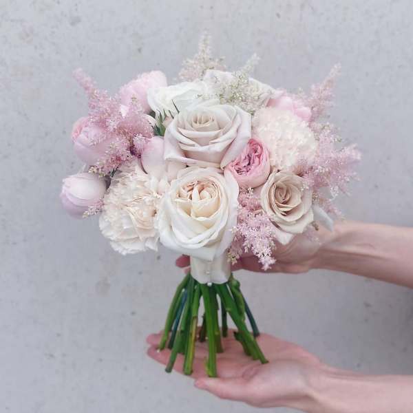 Handheld bouquet of pale pink and white roses with soft filler flowers