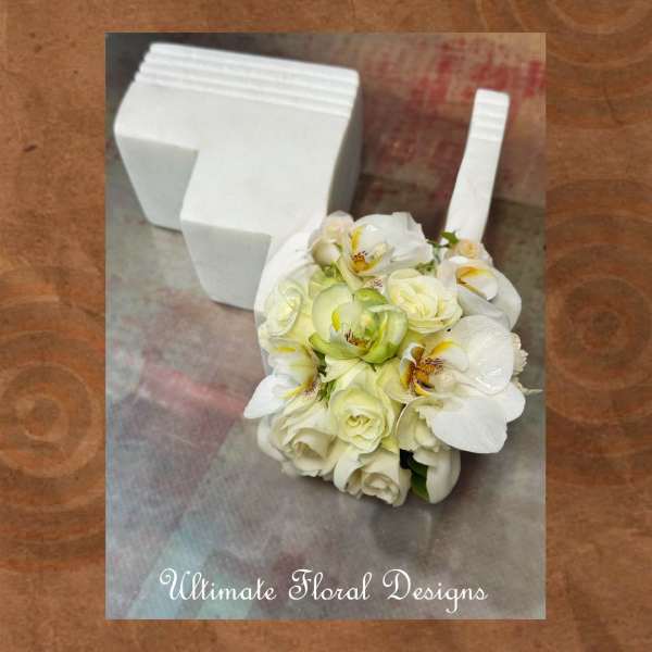 White floral bouquet with orchids and roses beside a white foam holder