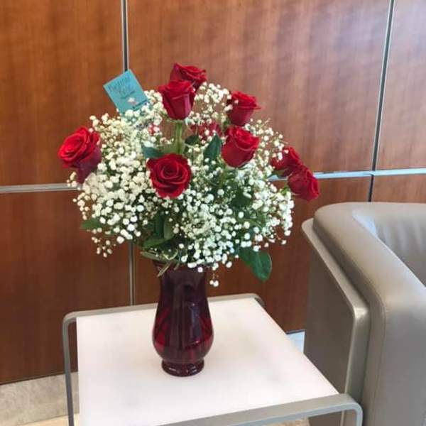 Red roses in a burgundy vase with white baby's breath