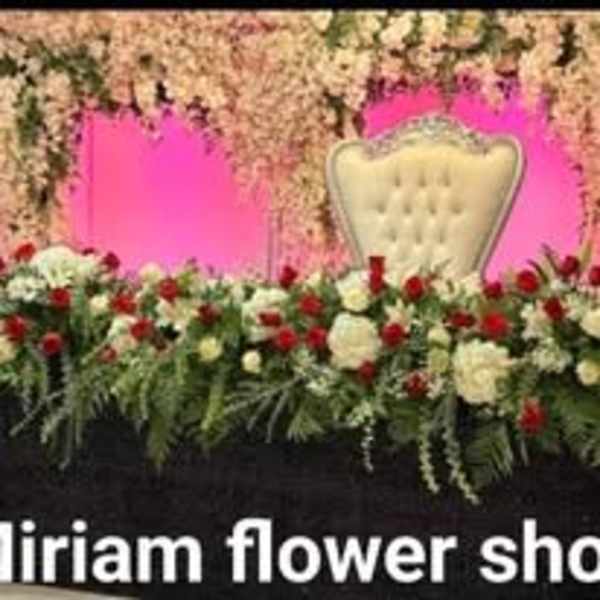 Floral stage backdrop with pink panels, a white chair, and red-white arrangements