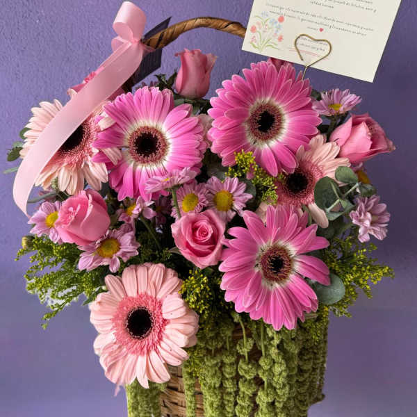 Pink gerbera daisies and roses in a wicker basket with a ribbon