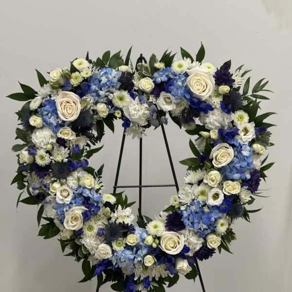 Heart-shaped floral wreath with blue, white, and cream flowers on a stand