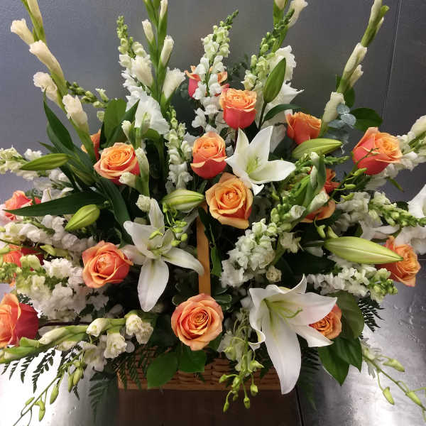 Large floral arrangement with orange roses, white lilies, and white spikes in a basket