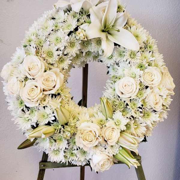White floral wreath on an easel with roses, lilies, and daisies
