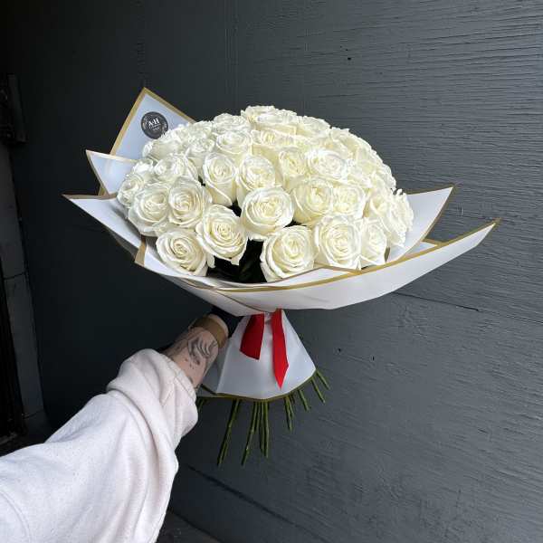 Large bouquet of white roses wrapped in white paper with a red ribbon