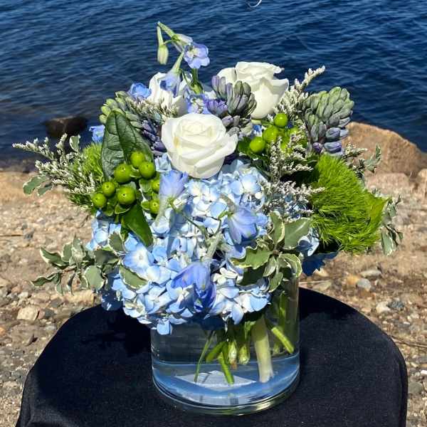 Blue and white floral arrangement in a glass vase by the water