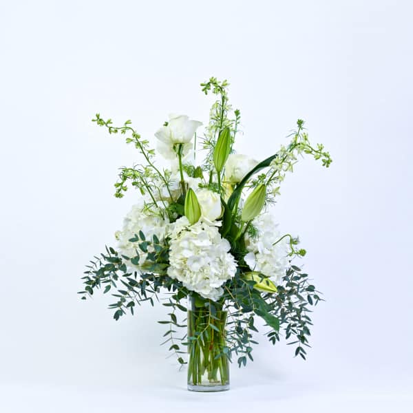 White floral arrangement in a clear glass vase with tall green accents