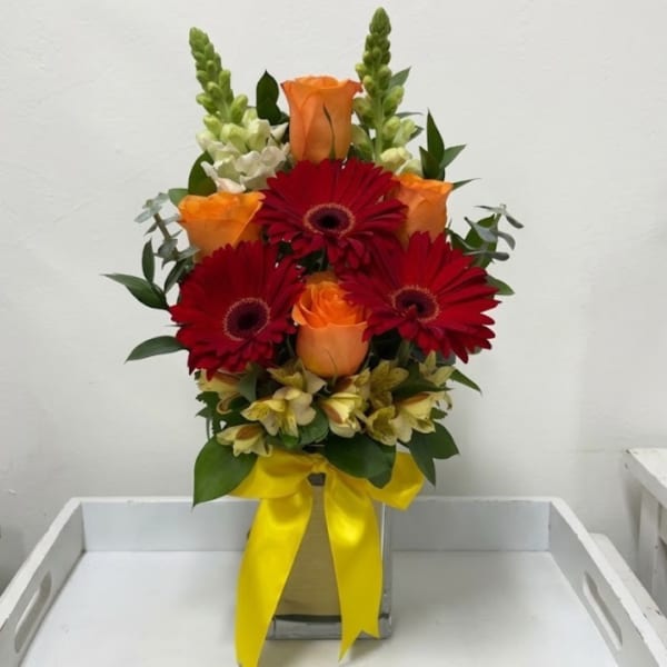 Bouquet of red gerbera daisies and orange roses in a vase with a yellow ribbon