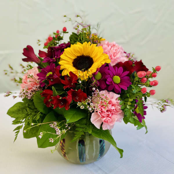 Mixed bouquet with a sunflower, carnations, and daisies in a glass vase