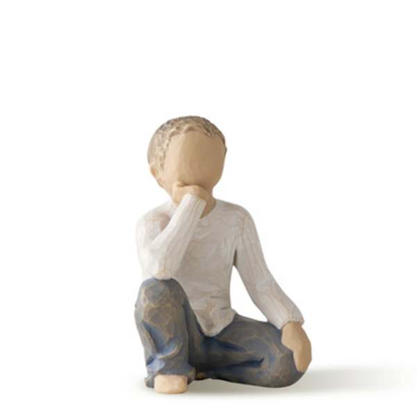 Small carved figurine of a seated child in a white shirt and blue pants
