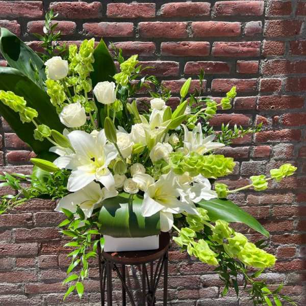 White lilies and roses arranged with bright green accents in a white vase