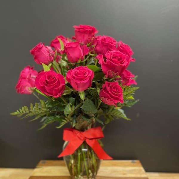 Tall arrangement of pink roses in a clear glass vase with a red bow