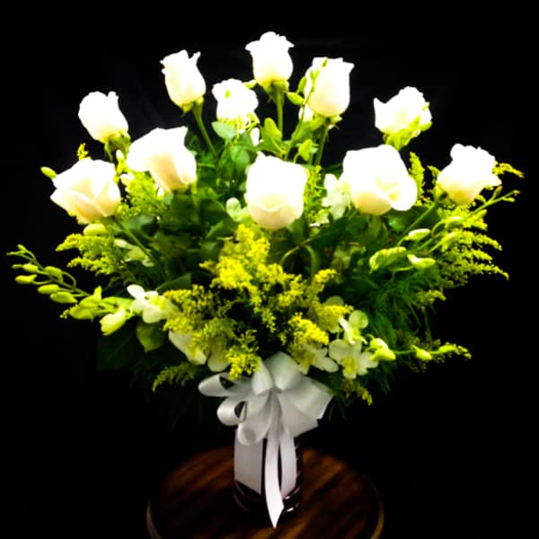 White roses arranged in a vase with yellow filler flowers and a white ribbon