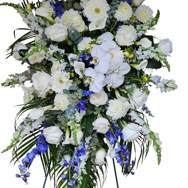 Tall white and blue funeral spray with roses, orchids, and daisies