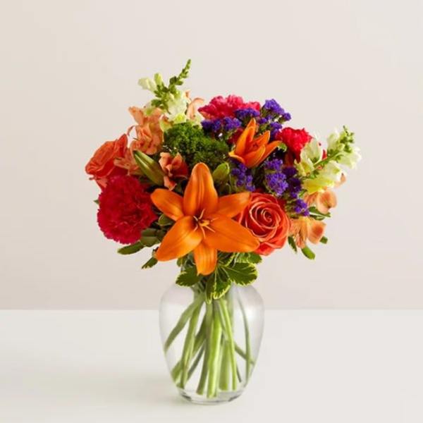 Colorful bouquet of lilies, roses, and carnations in a clear glass vase