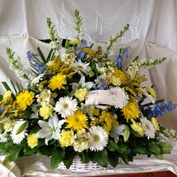 Large mixed floral arrangement in a white basket with yellow, white, and blue blooms