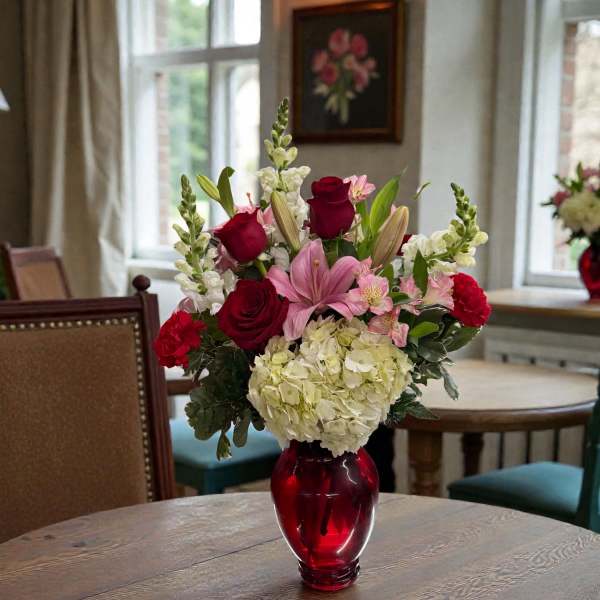Mixed pink and red flowers in a red glass vase on a table