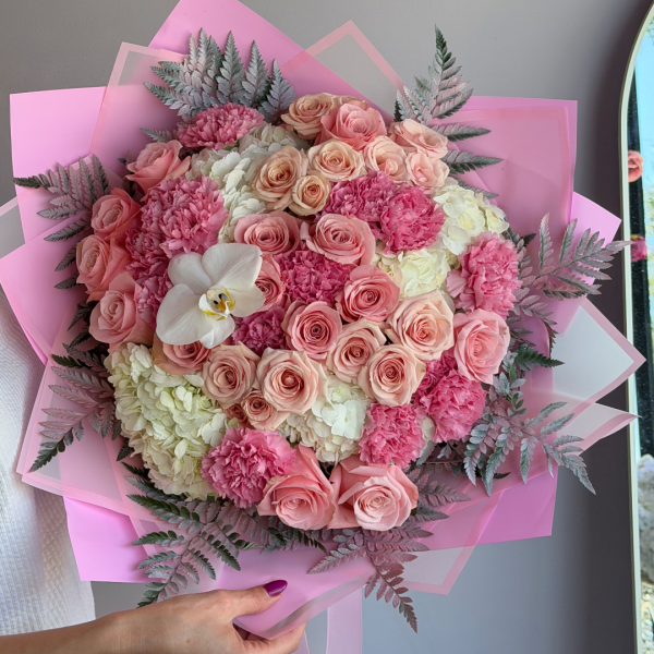 Pink and cream bouquet of roses, carnations, and hydrangeas wrapped in pink paper
