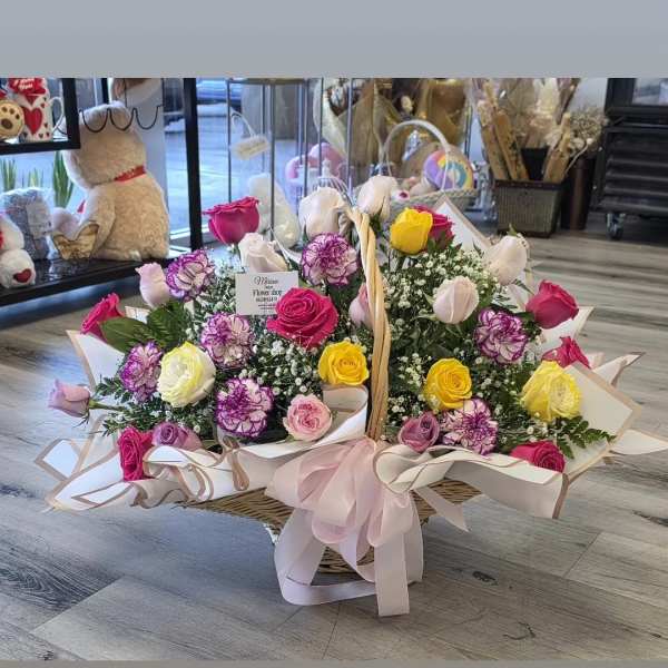 Basket arrangement of multicolored roses and carnations with a pink ribbon