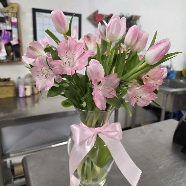 Pink tulips and alstroemeria in a glass vase with a pink ribbon